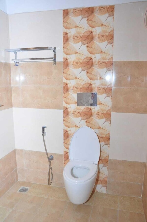 A bathroom with a toilet, a handrail, and a shower.