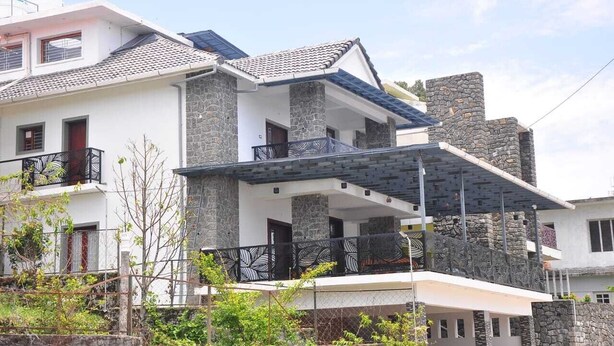 Een huis met twee verdiepingen, een stenen gevel, een balkon met metalen hekwerk en een plat dak.