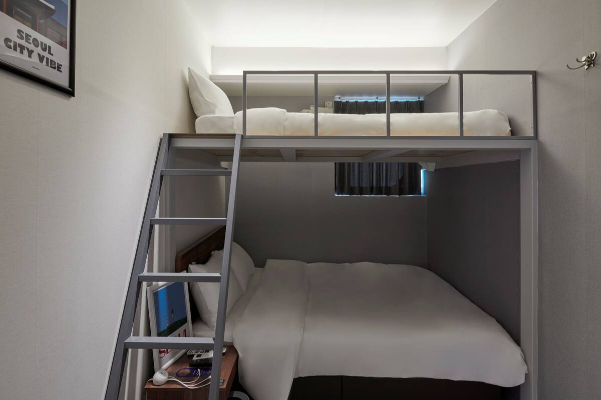 Uma cama beliche com escada, uma janela pequena e um quadro na parede.