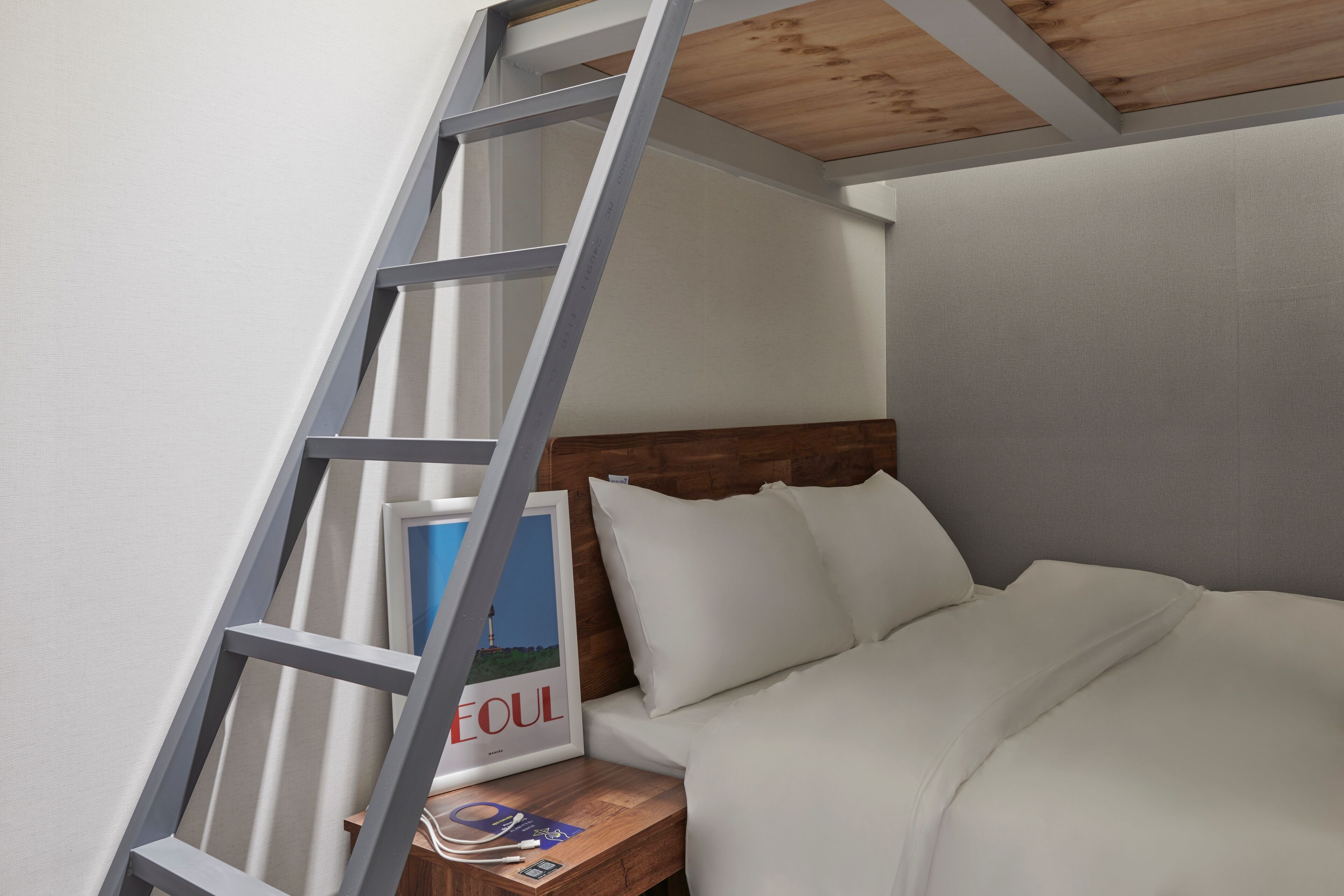 Une chambre à coucher avec une tête de lit en bois, une échelle et un tableau encadré posé sur la table de chevet.