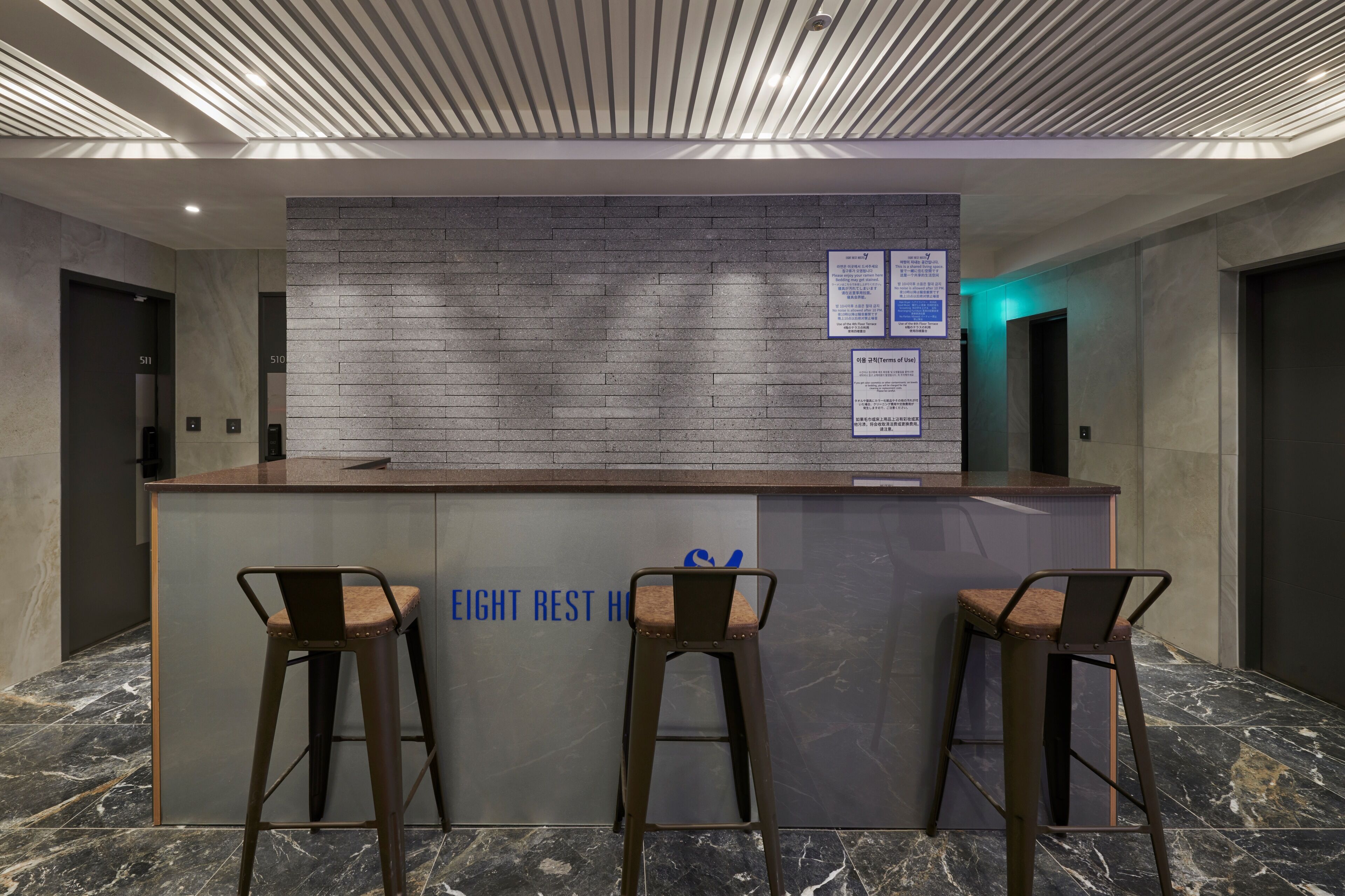 Een receptiebalie met een modern ontwerp, twee barkrukken en een bord met de tekst 'EIGHT REST HOU'.