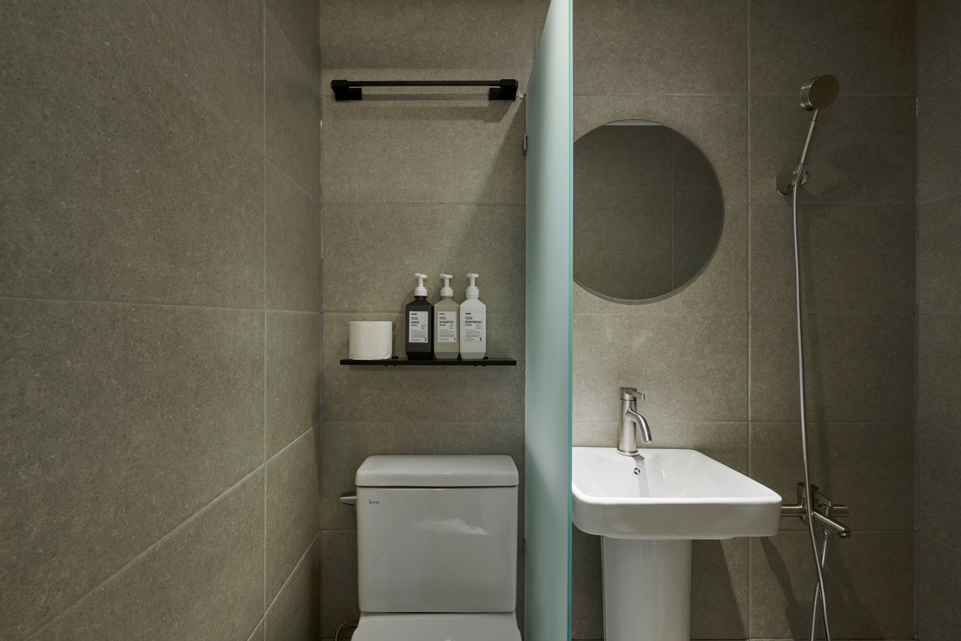 Une salle de bain moderne avec des toilettes, un lavabo et une douche. On trouve des articles de toilette sur une étagère.