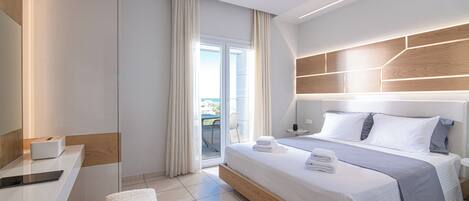 A modern hotel room with a large bed, a bedside table, a desk, and a view of the outdoors.