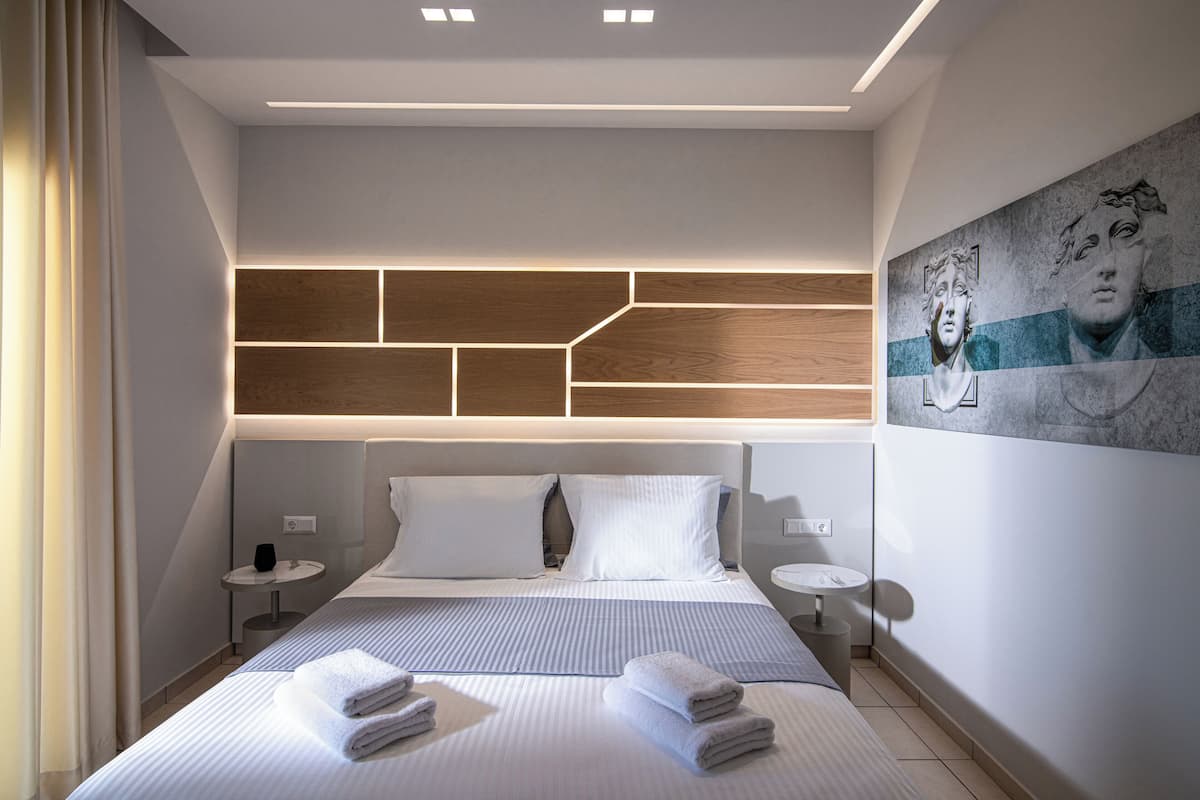 A modern hotel room with a large bed, two bedside tables, a headboard with geometric wooden panels, and a wall-mounted artwork.