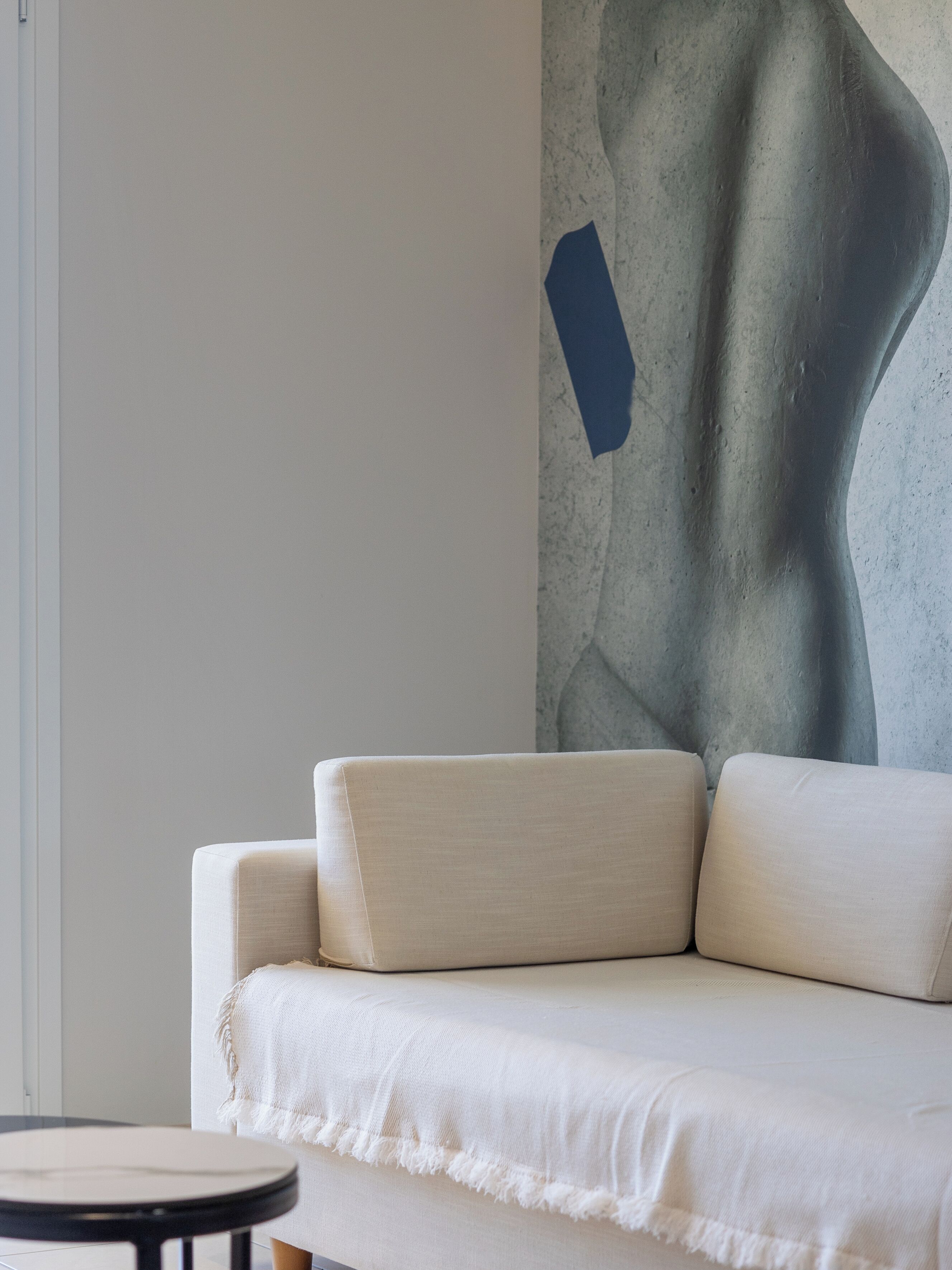 Un salon moderne avec un canapé, une table ronde et un mur orné d’un tableau abstrait aux textures marquées.