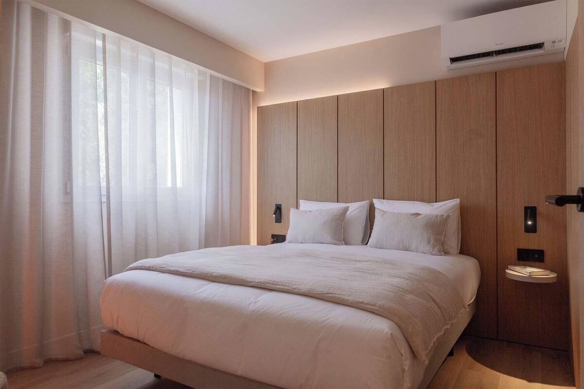 Un dormitorio moderno con una cama grande, paneles de madera en las paredes y un equipo de aire acondicionado.