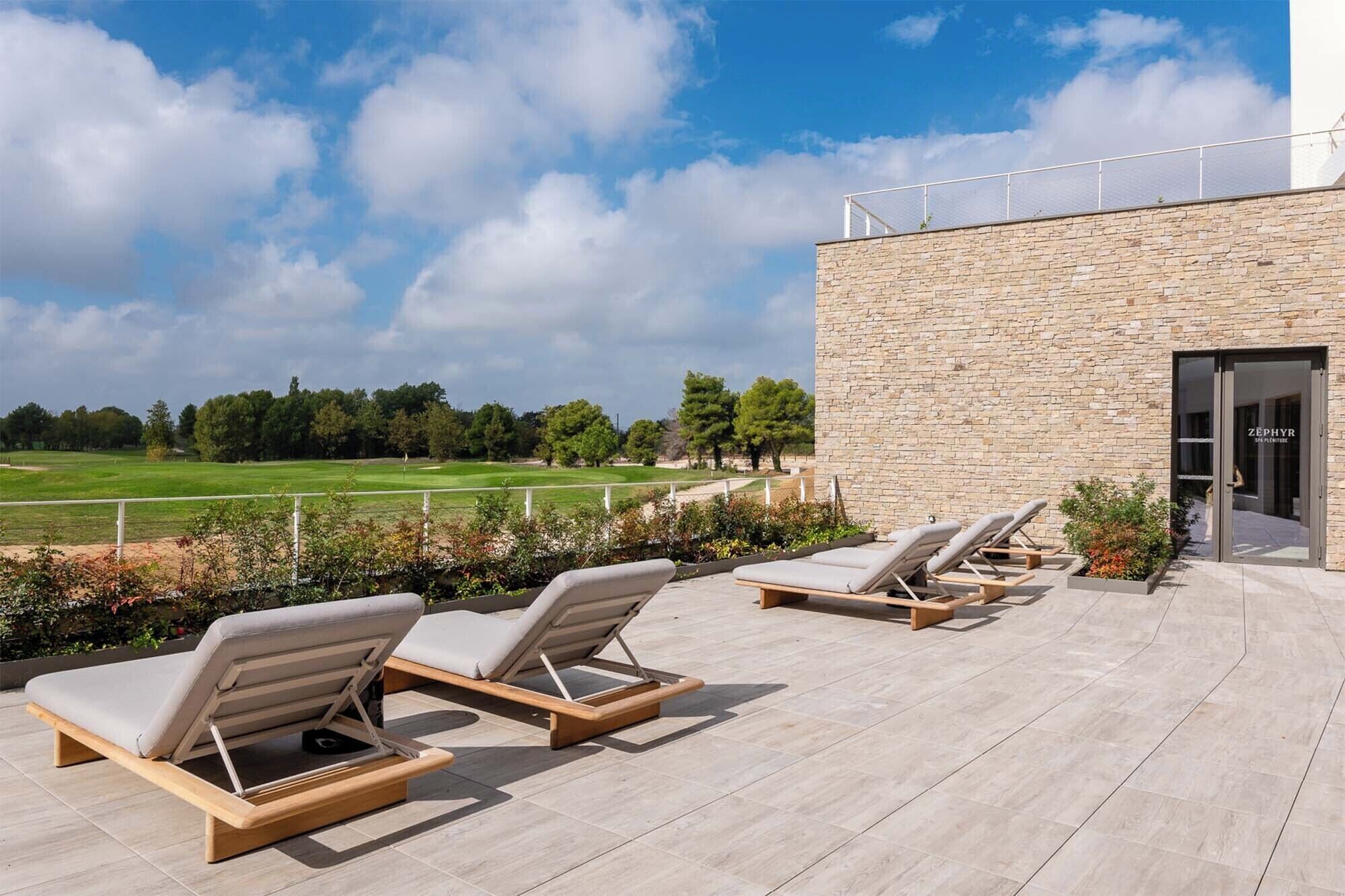 Eine Dachterrasse mit Liegestühlen, ein Steinhaus und Blick auf einen Golfplatz.