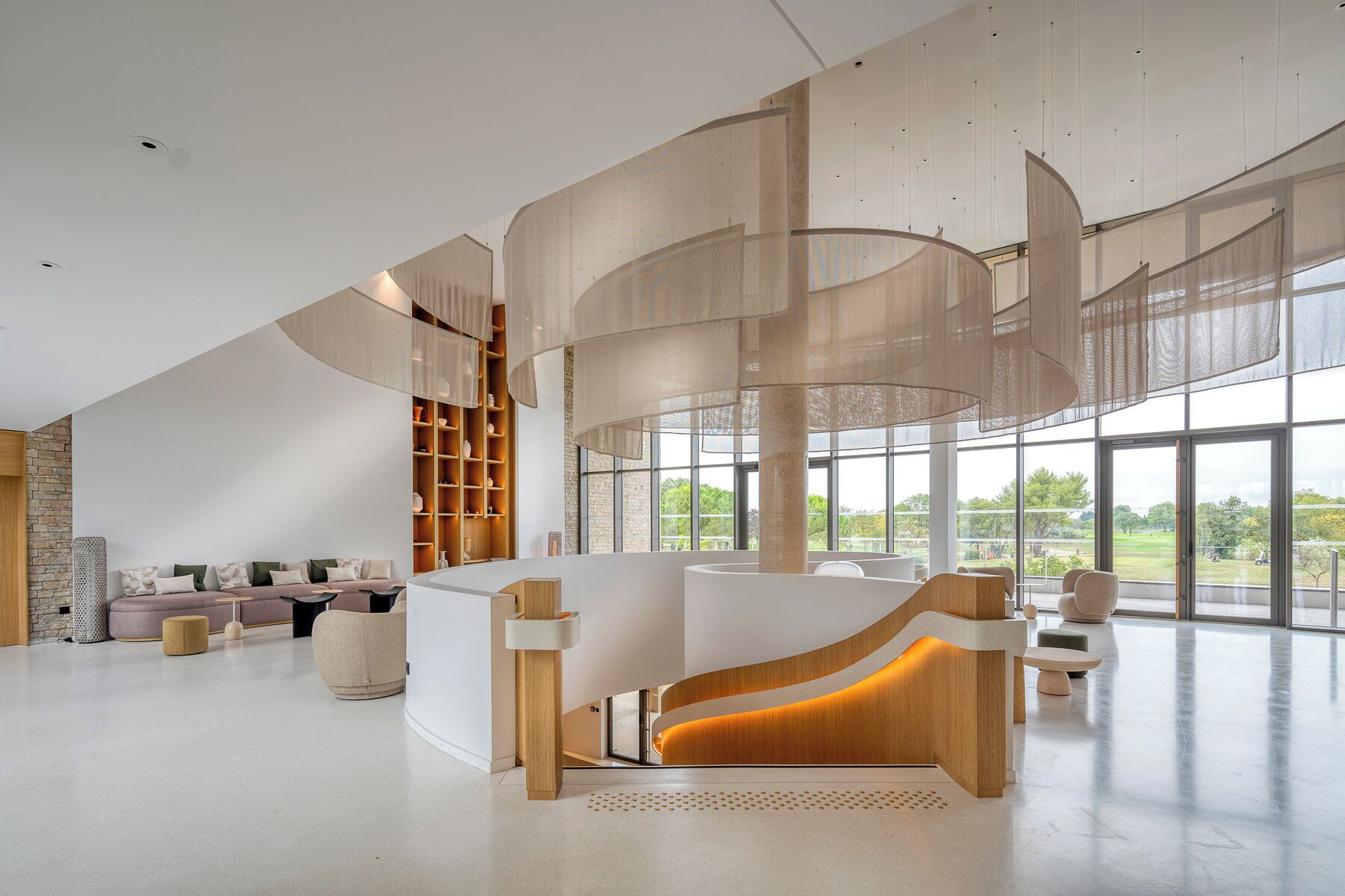 A spacious lobby with a curved reception desk, a seating area with sofas, and large windows offering a view of the outdoors.