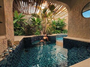 A woman relaxing in a small, tiled indoor pool with tropical plants and a decorative ceiling. - Udaya Resort (Palakkad)