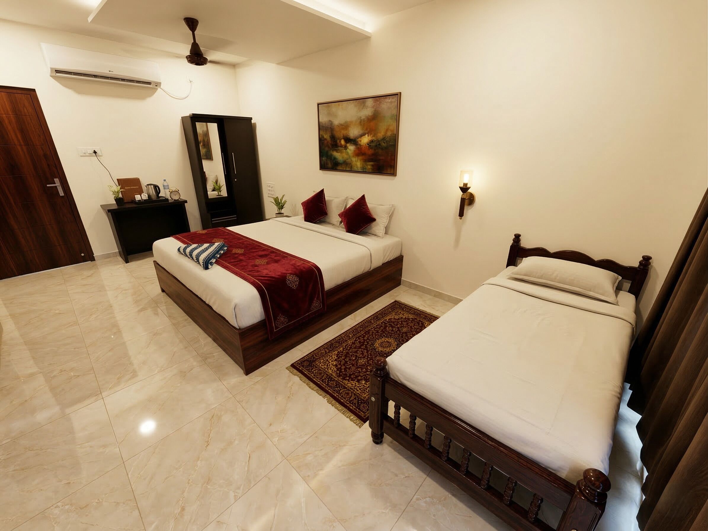 A hotel room with two beds, a desk, a mirror, an air conditioner, a painting, and a ceiling fan.