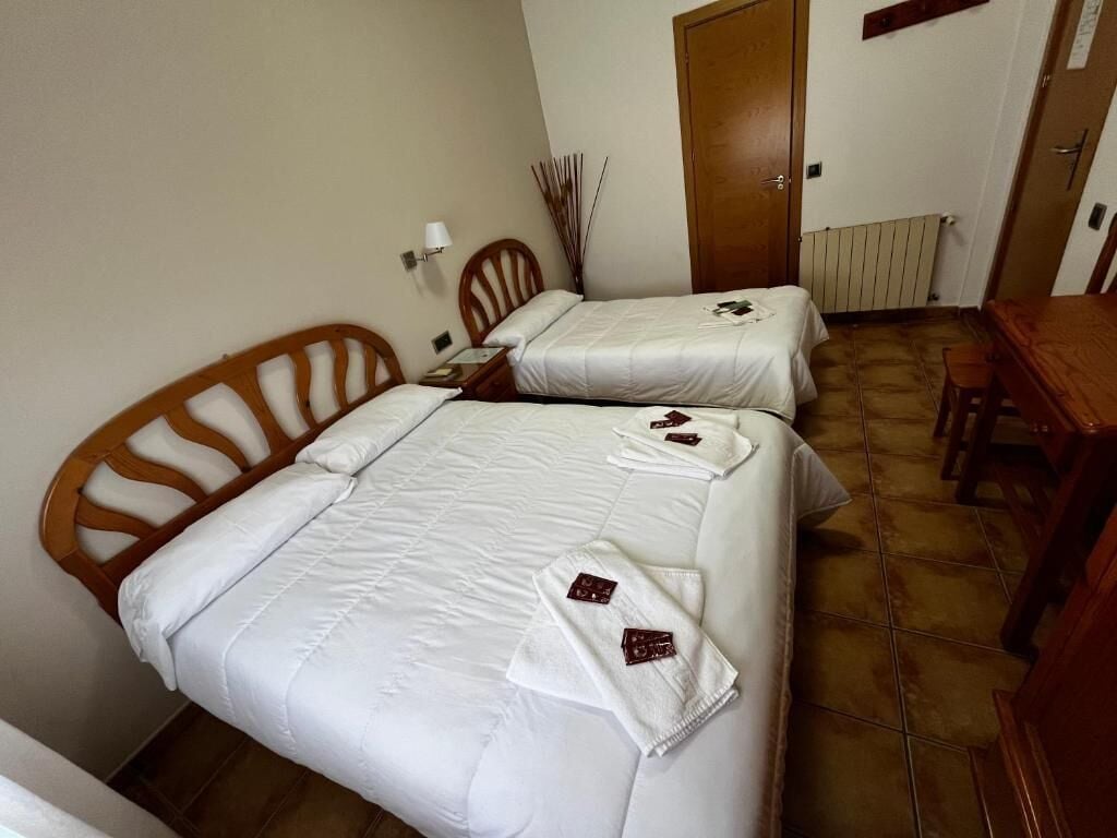 Two single beds with white linens and towels, a wooden chair, a wooden table, and a radiator.