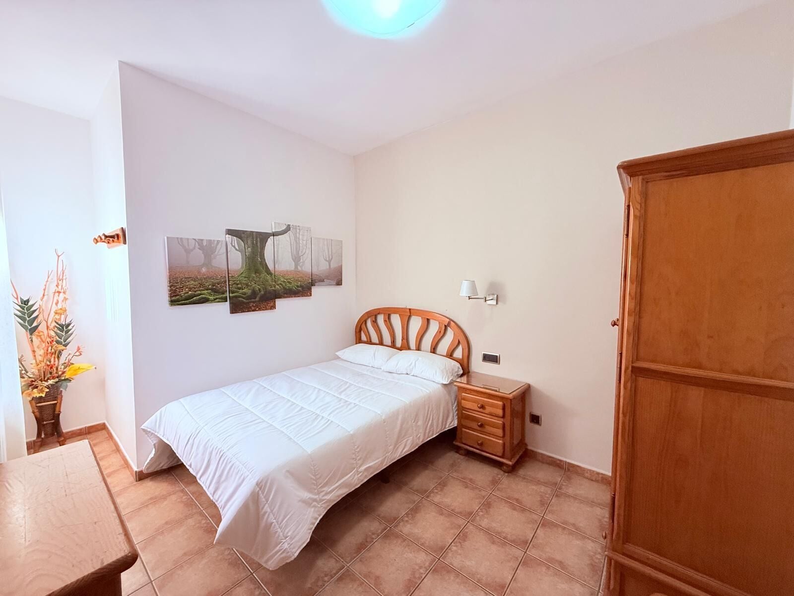 Un dormitorio con cama, mesita de noche, lámpara, armario y decoración en la pared.