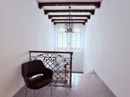 Una habitación con una silla negra, un portón de hierro forjado y una ventana con persianas.