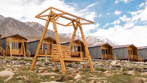 A wooden swing set in a mountainous area with several wooden cabins in the background. - Falcon'S Cottages (Leh)