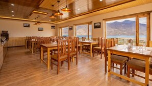 A restaurant with wooden furniture and large windows offering a mountain view. - Falcon'S Cottages (Leh)