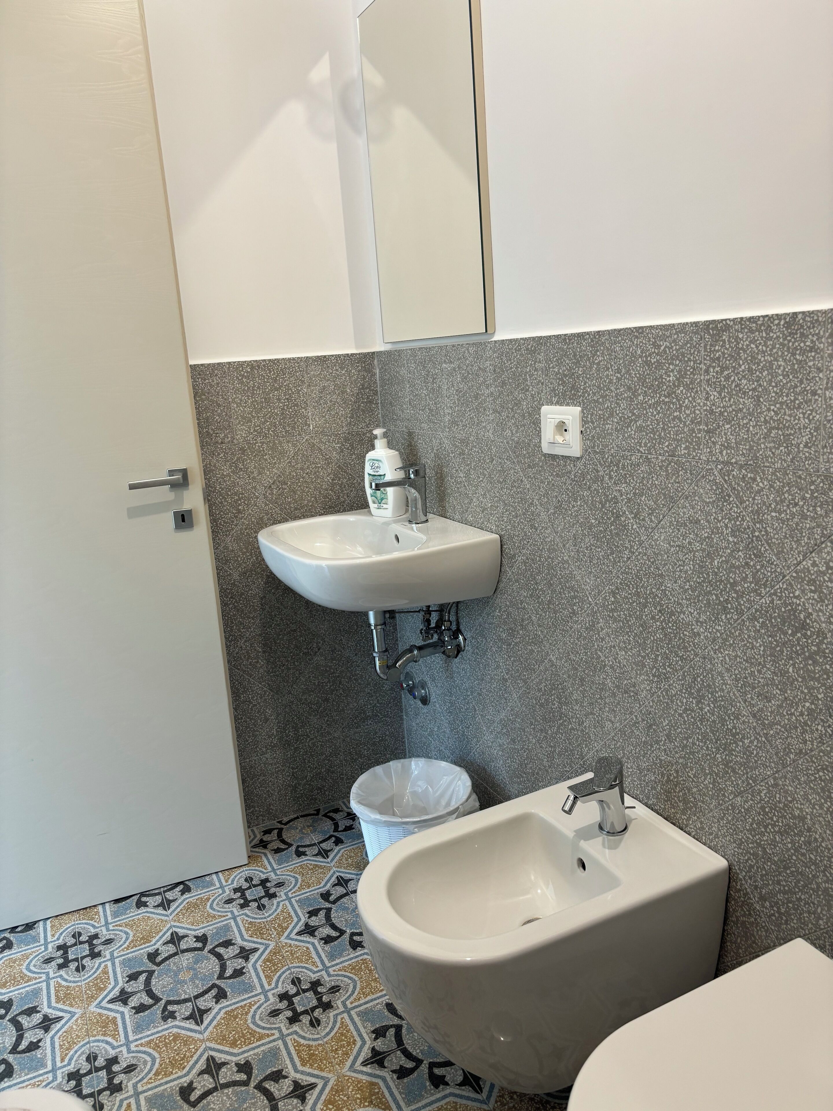 A bathroom with a white sink, a bidet, a toilet, and a trash bin.