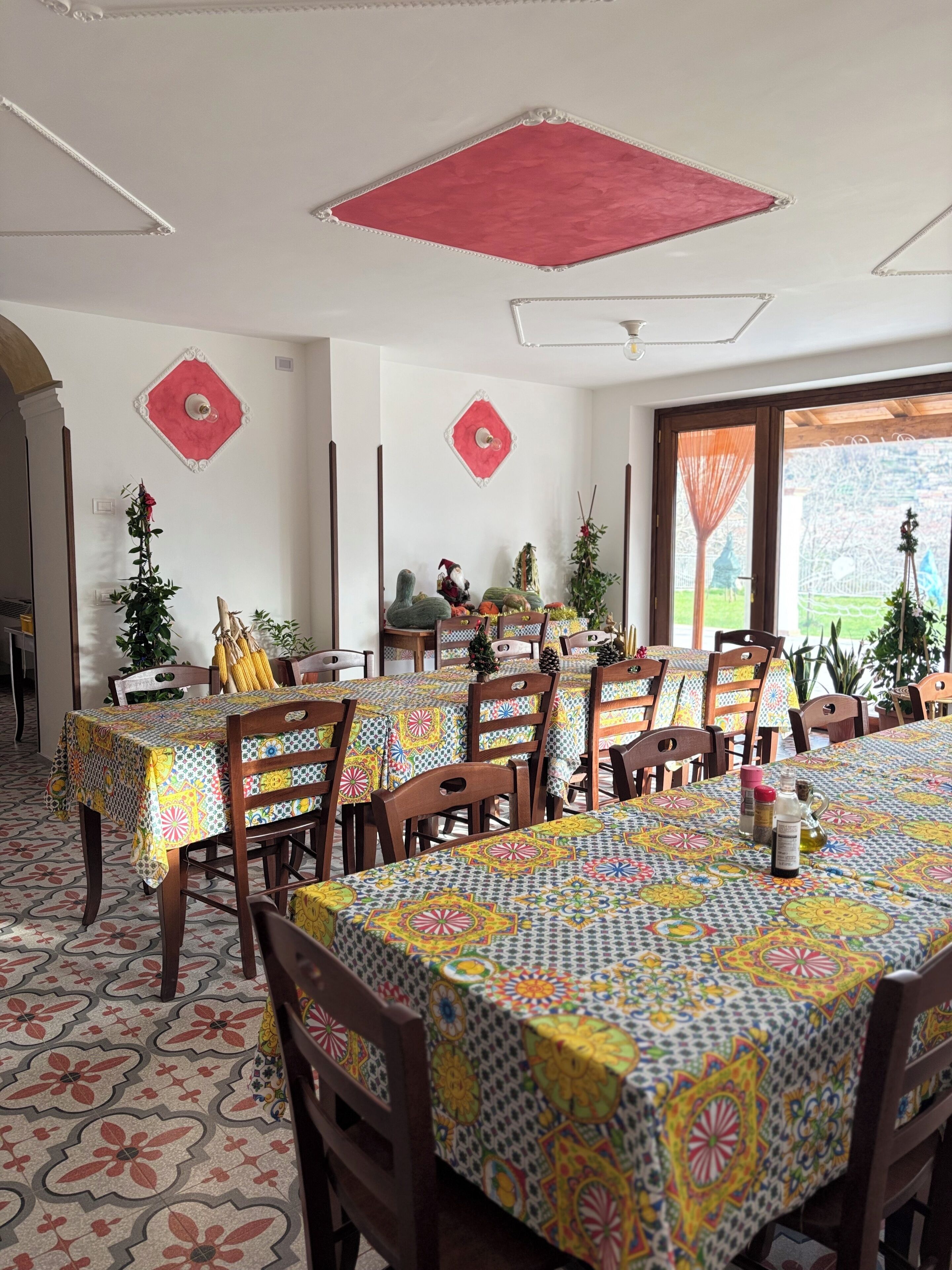 Un comedor con varias mesas cubiertas con manteles coloridos, sillas de madera y elementos decorativos en las paredes.