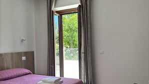 Habitación de hotel con cama, una silla, ventana con cortinas y vistas a zonas verdes.