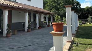Un edificio con un patio techado, plantas en macetas y un césped.