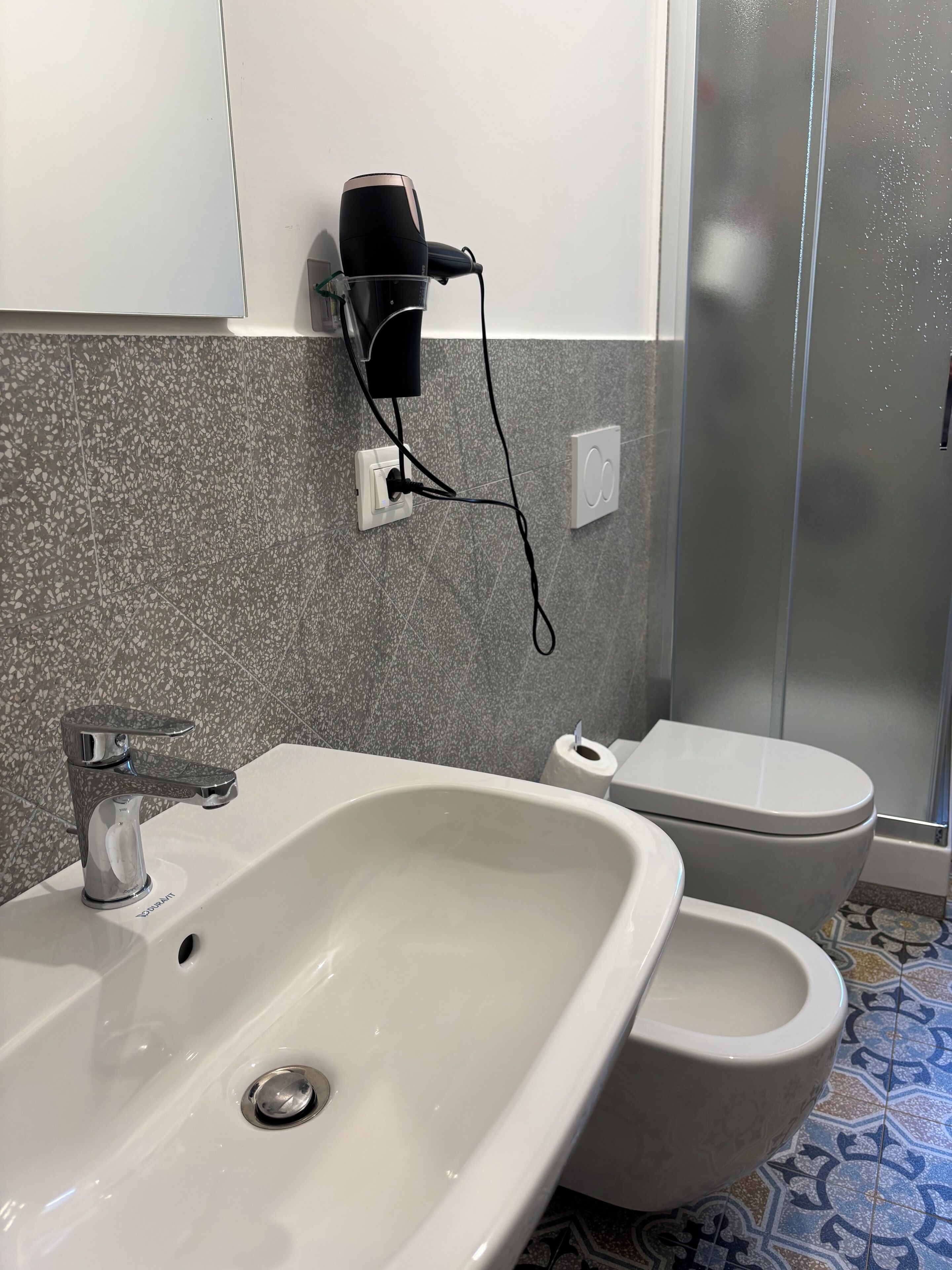 Ein Badezimmer mit Waschbecken, Toilette und einem an der Wand angeschlossenen Fön.