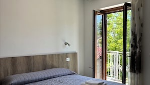 Un dormitorio con cama, cabecera de madera, ventana con vistas a zonas verdes y suelo de baldosas estampadas.