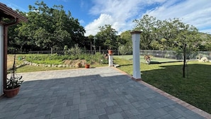 Un patio empavedado con piso de ladrillo, rodeado por una valla metálica y follaje.