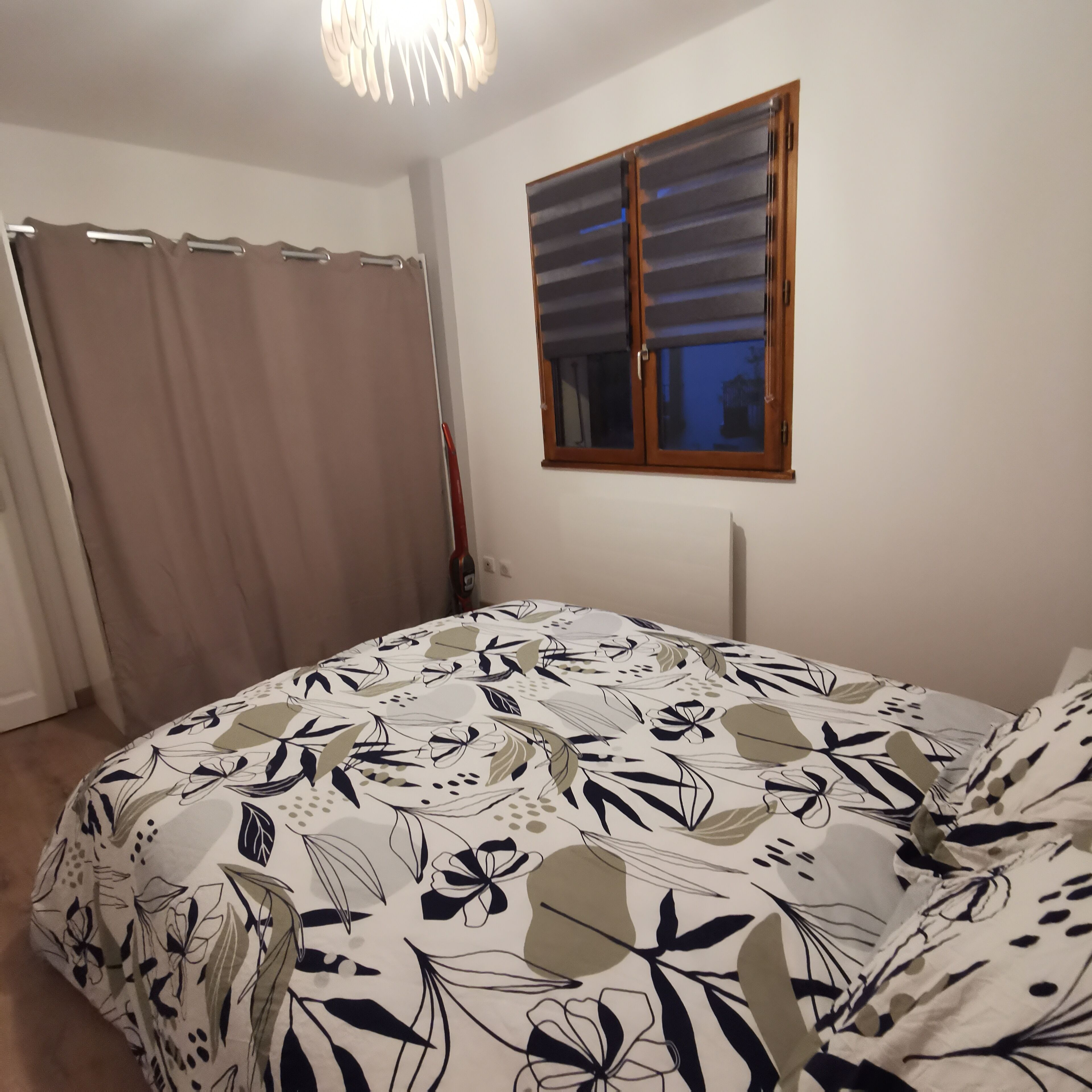 Een slaapkamer met een bed, gordijnen, een raam en een plafondlamp.