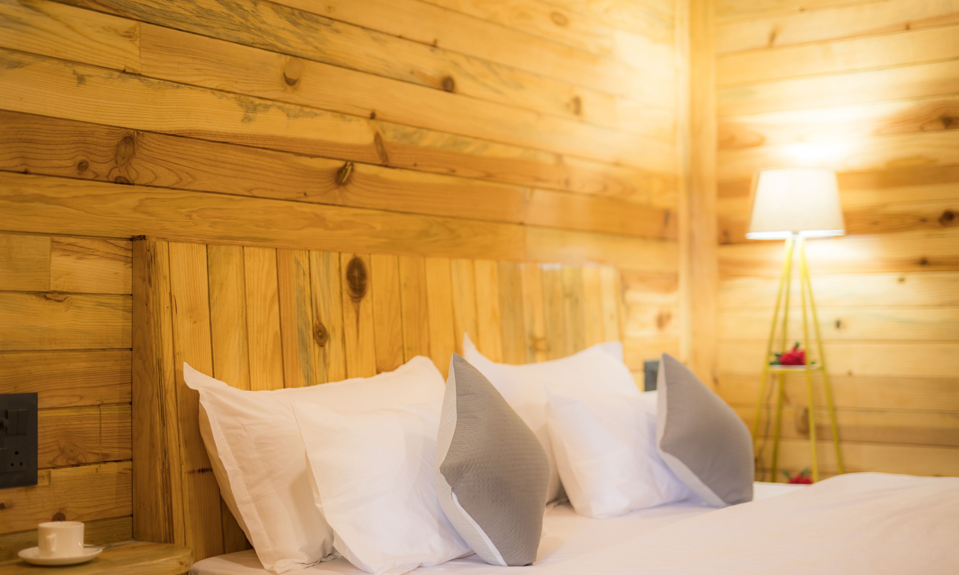 A wooden cabin room with a bed, pillows, a bedside table, and a lamp.