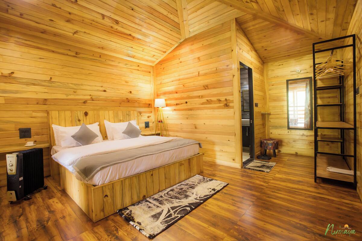 A wooden cabin bedroom with a bed, bedside table, lamp, radiator, and a wooden ladder.