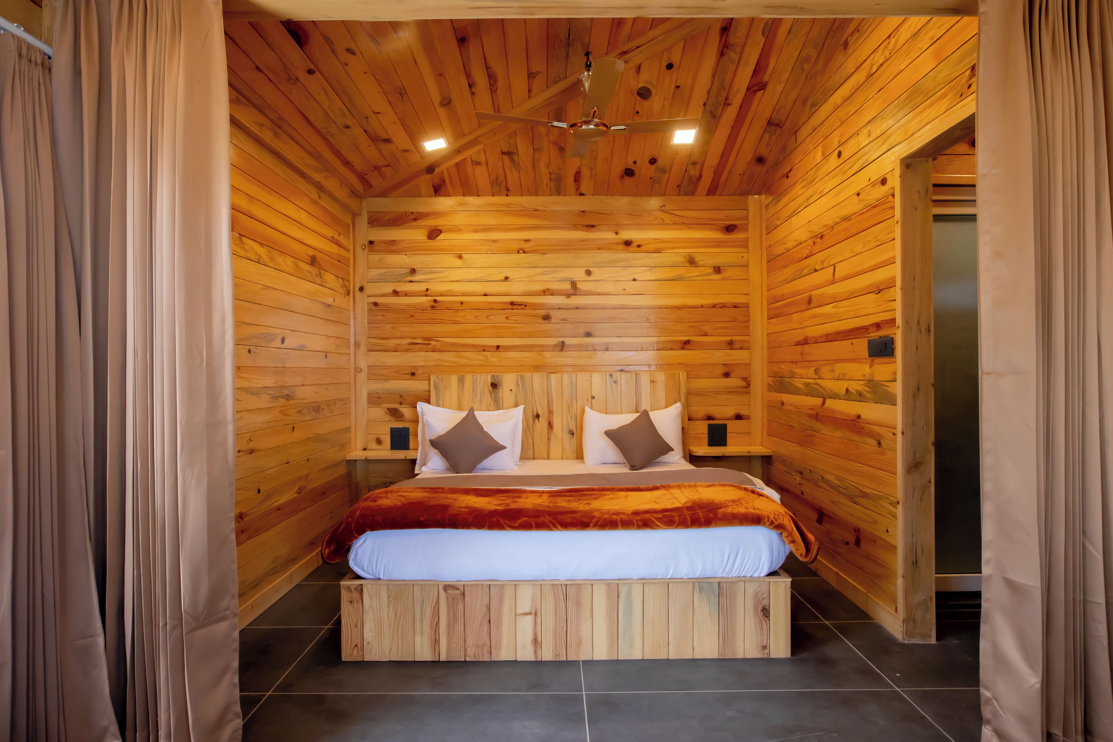 Un dormitorio con paneles de madera, una cama, un ventilador de techo y una mesita de noche.
