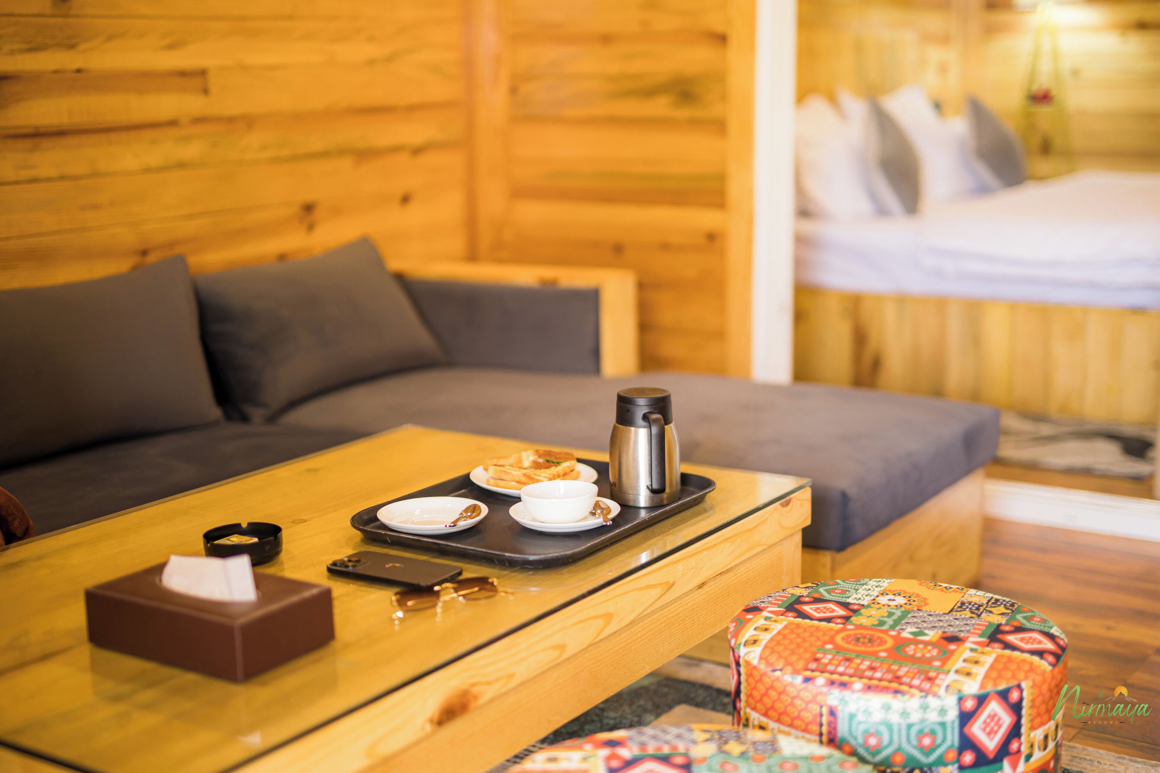 Ein Holzinterieur mit einer Couch, einem kleinen Tisch mit Frühstücksangebot und einem farbenfrohen Pouf.