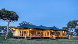A large, open-air structure with a covered porch and multiple seating areas, surrounded by natural landscape. - The African Kongoni Serengeti Safari Camp (Serengeti)