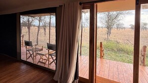 Una habitación amplia con piso de madera, un gran ventanal corredero que da a una terraza exterior y vistas de un paisaje natural.