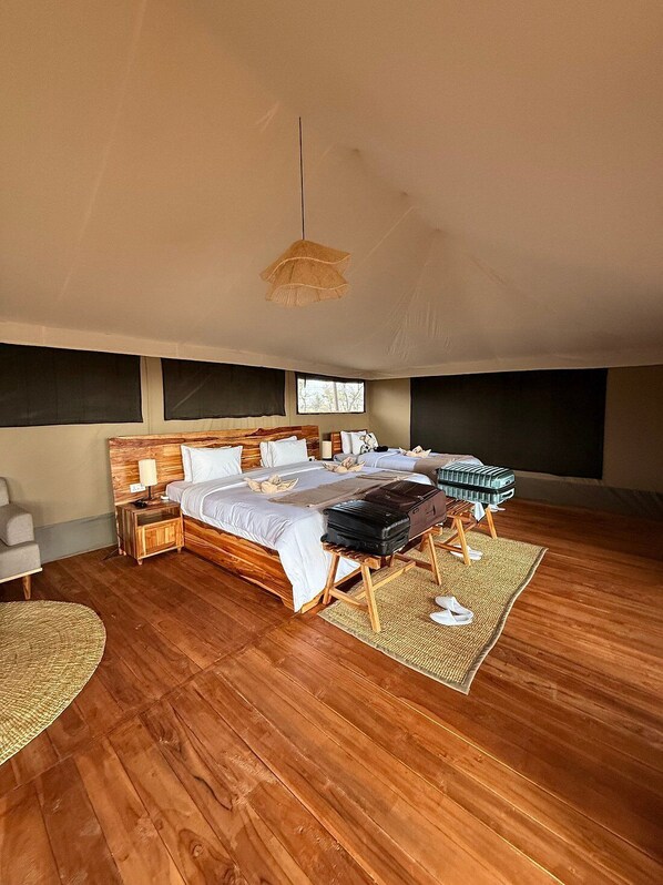 A spacious bedroom with a large bed, wooden headboard, and a suitcase on a wooden stand. - The African Kongoni Serengeti Safari Camp (Serengeti)