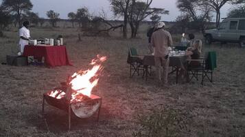 A group of people dining outdoors with a fire pit in the foreground.