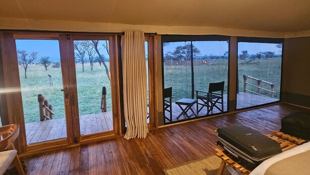 Un dormitorio con ventanas amplias, una cama, suelo de madera y una lámpara colgante.