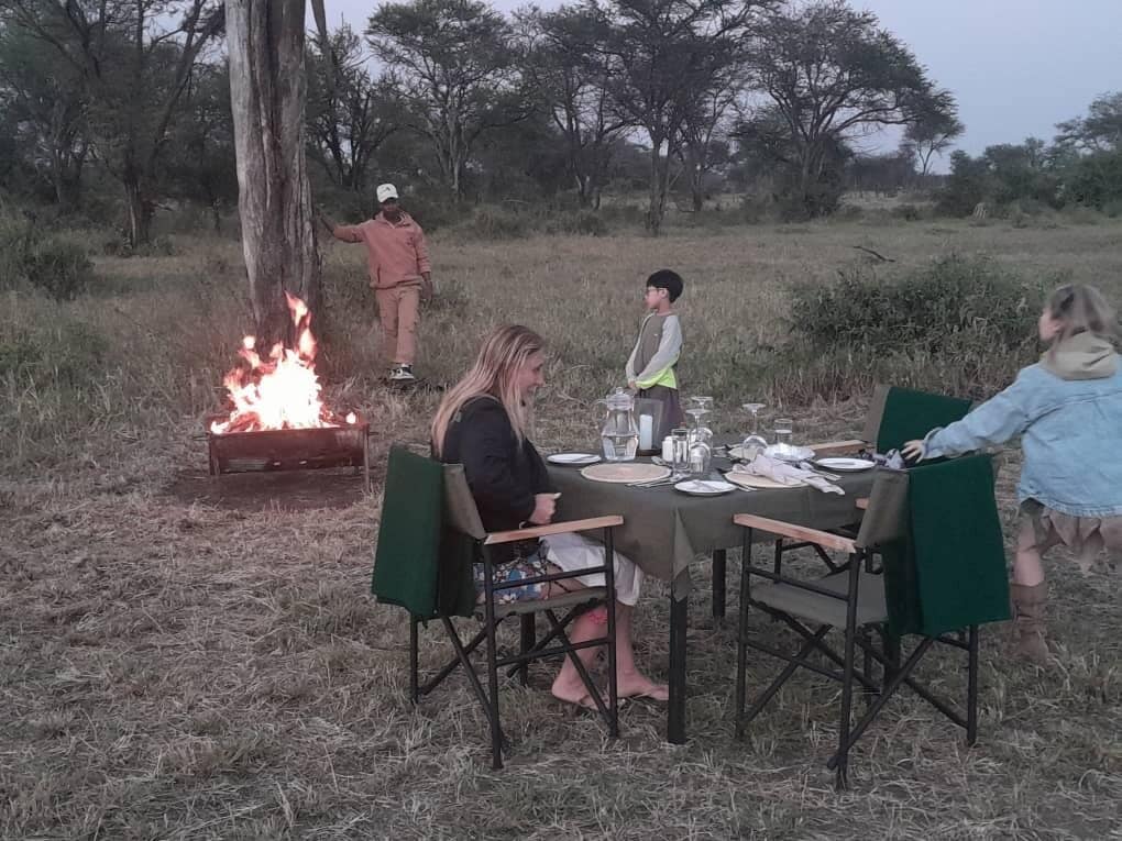 Un groupe de personnes est réuni autour d’un brasero, en plein air, pour dîner.
