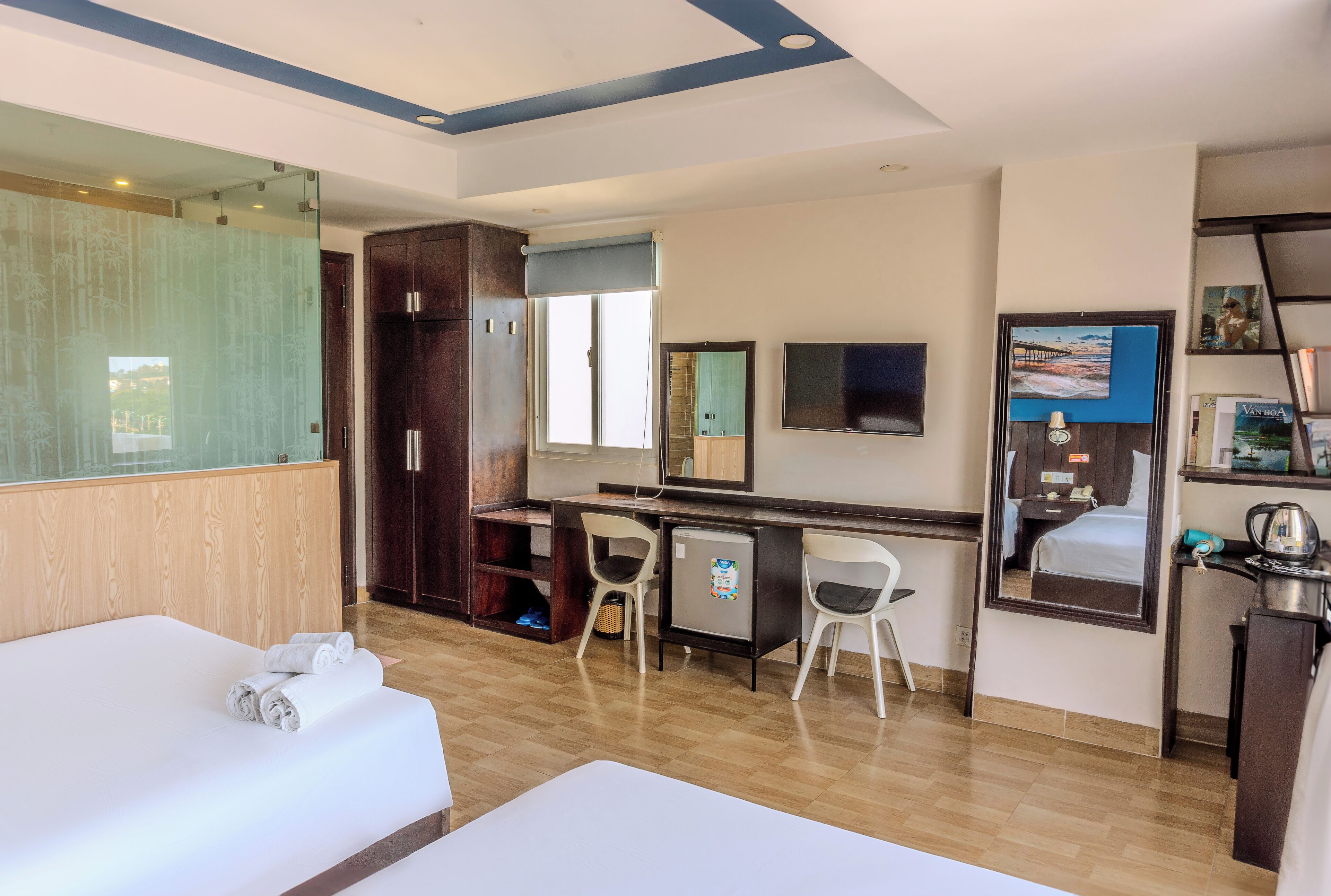 Una habitación de hotel con cama, escritorio, silla, espejo y un refrigerador pequeño.