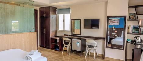 Una habitación de hotel con cama, escritorio, silla, espejo y un refrigerador pequeño.