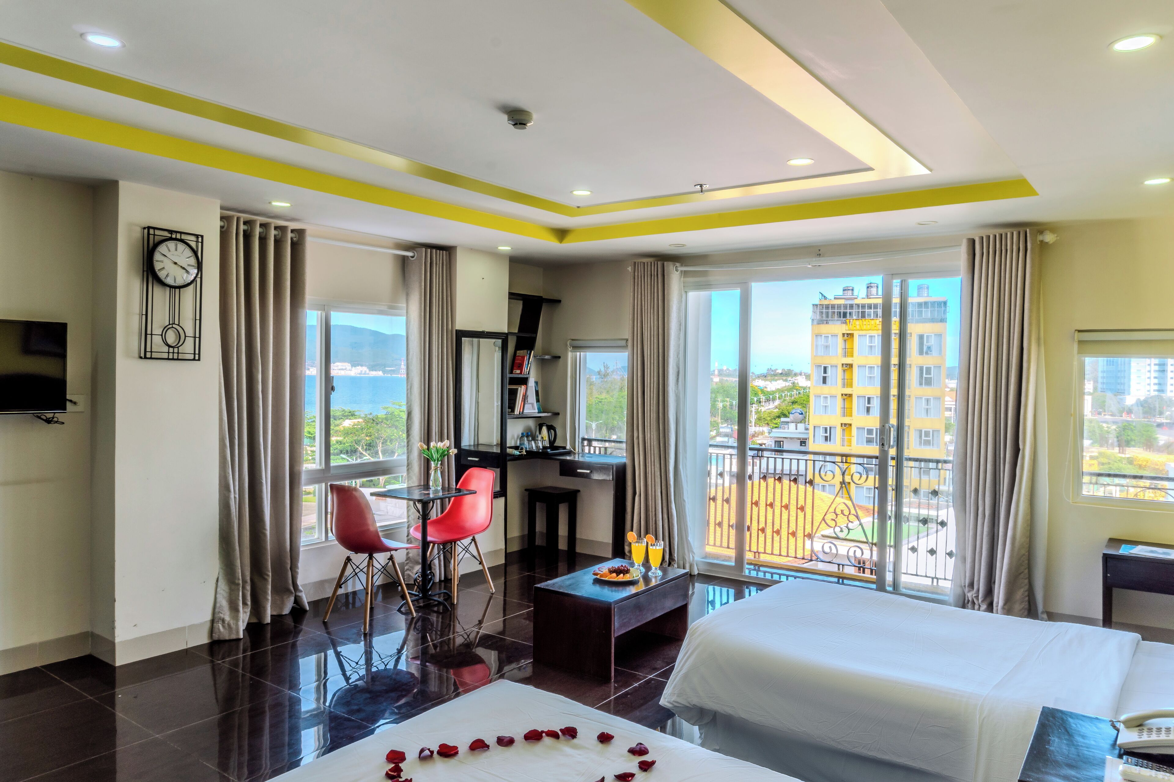A hotel room with a bed, a desk, a chair, a TV, and a balcony with a view of the city.