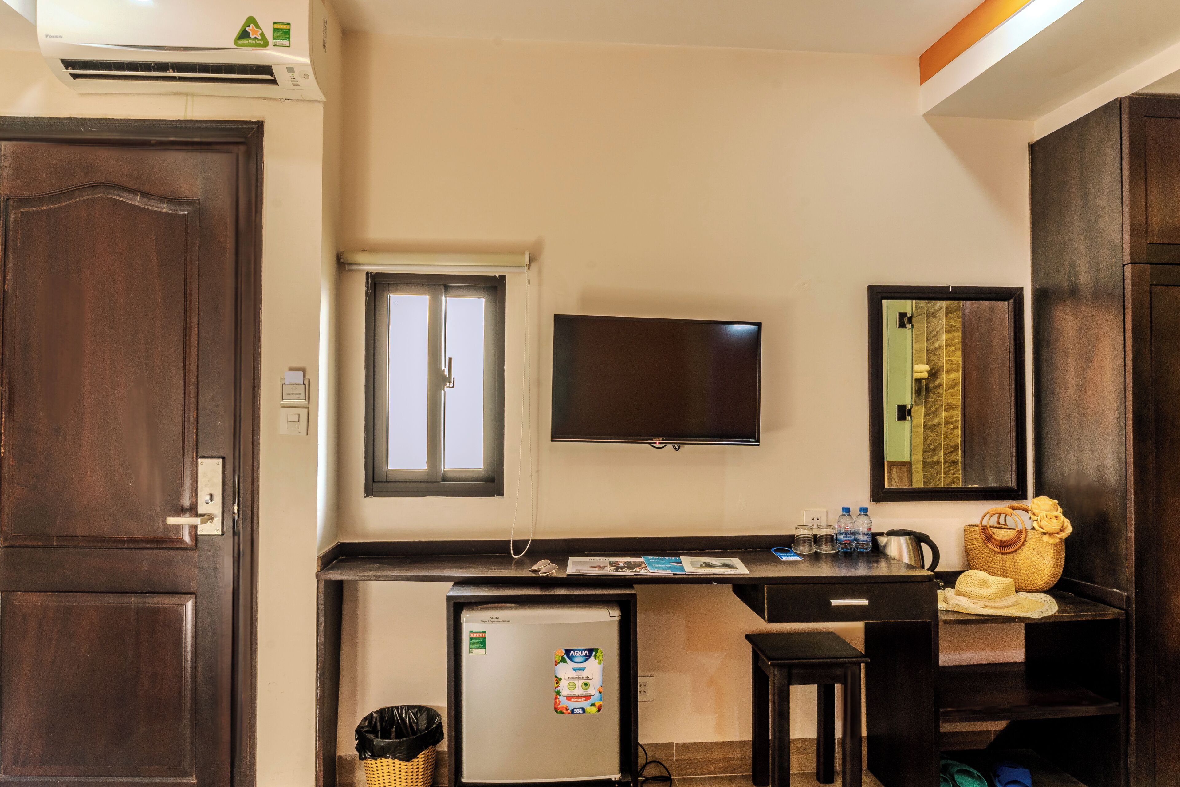 Ein kompaktes Hotelzimmer mit Küchenzeile, Flachbildfernseher, kleinem Kühlschrank, Schreibtisch und Spiegel.