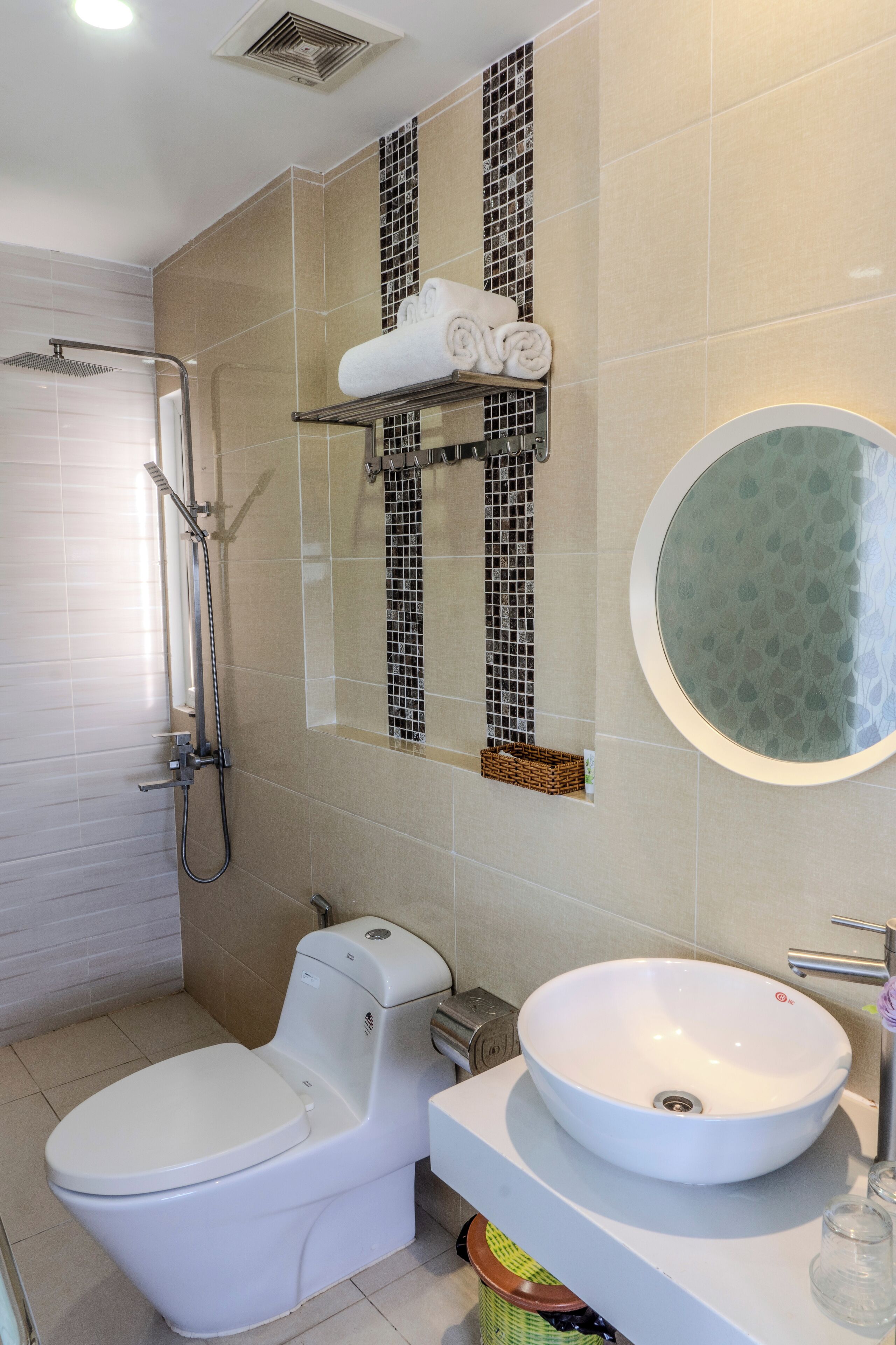 Een badkamer met toilet, wastafel en douche. Handdoekrek met handdoeken en een spiegel boven de wastafel.