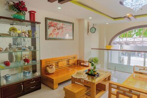 A cozy living area with a wooden bench, a glass display cabinet, and a dining table with a vase of flowers. - Melyna Hotel Nha Trang Beach (Nha Trang)
