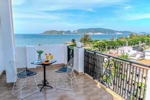 A balcony with a table, two chairs, and a view of the sea and distant hills. - Melyna Hotel Nha Trang Beach (Nha Trang)