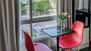 A room with a table and two red chairs, a vase with flowers, and a view of the sea and mountains through large windows. - Melyna Hotel Nha Trang Beach (Nha Trang)