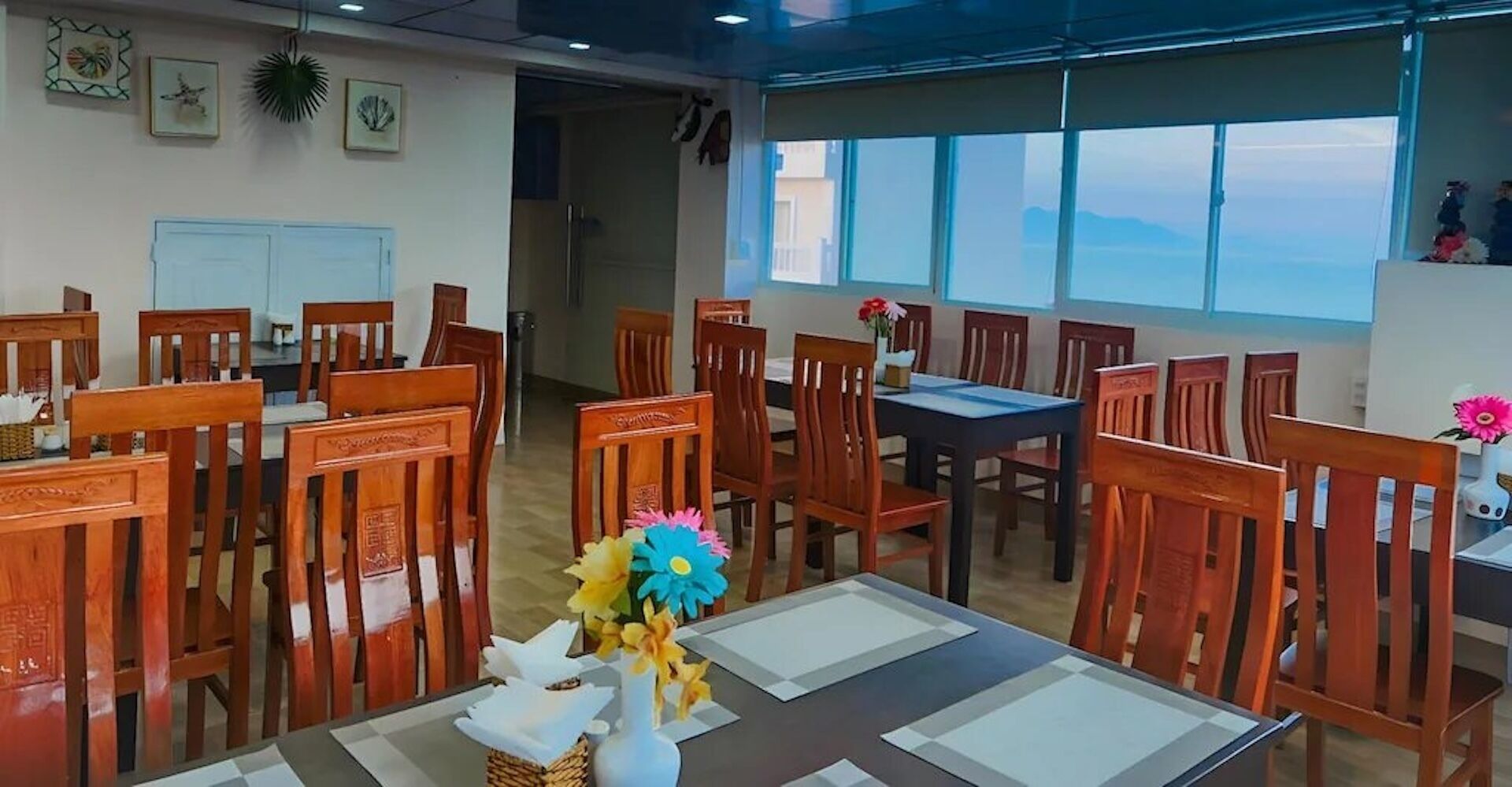 Un comedor con sillas y mesas de madera, un ventanal con vistas y decoración en la pared.