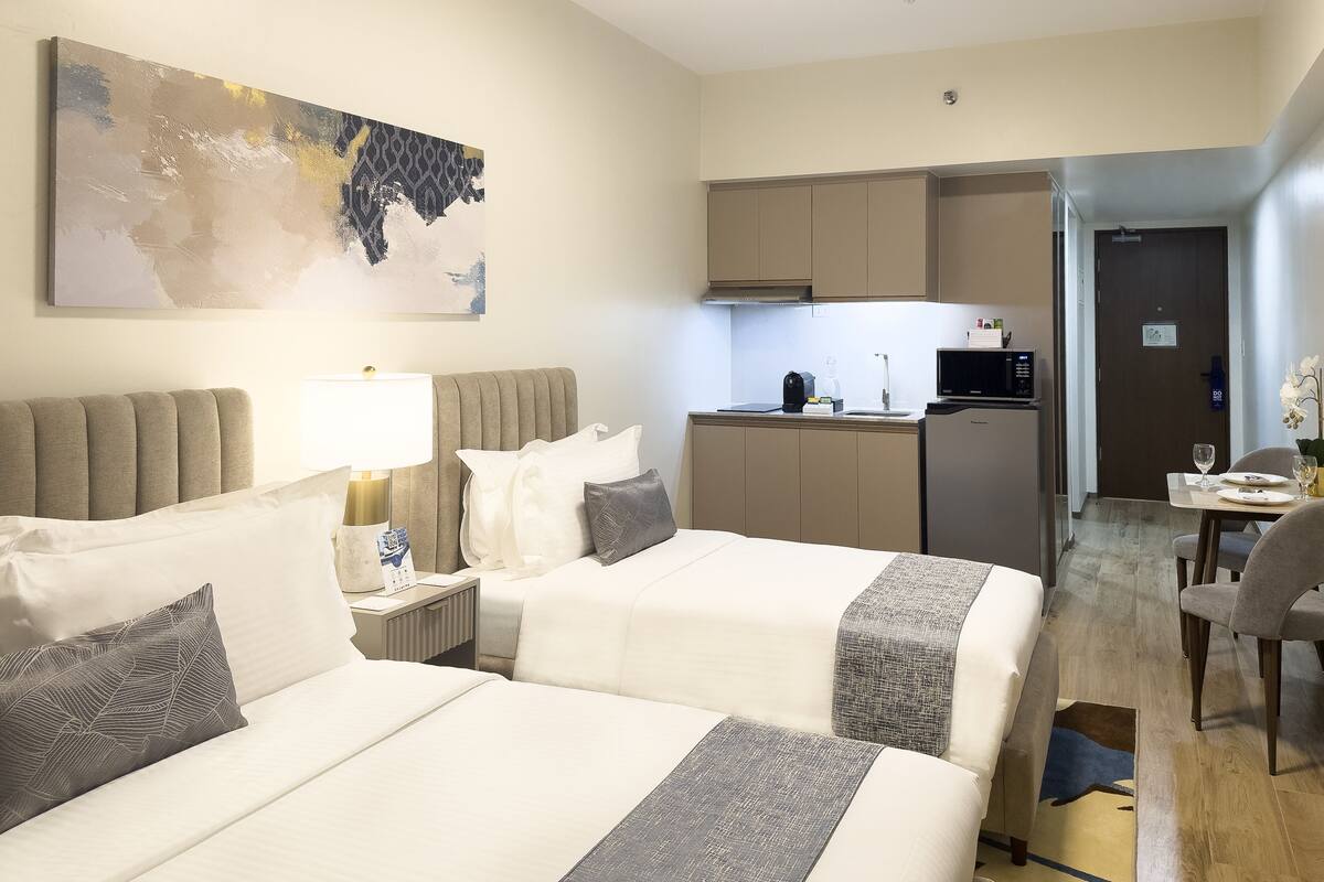 Una habitación de hotel con dos camas, una kitchenette pequeña, un rincón de comedor y un cuadro en la pared.