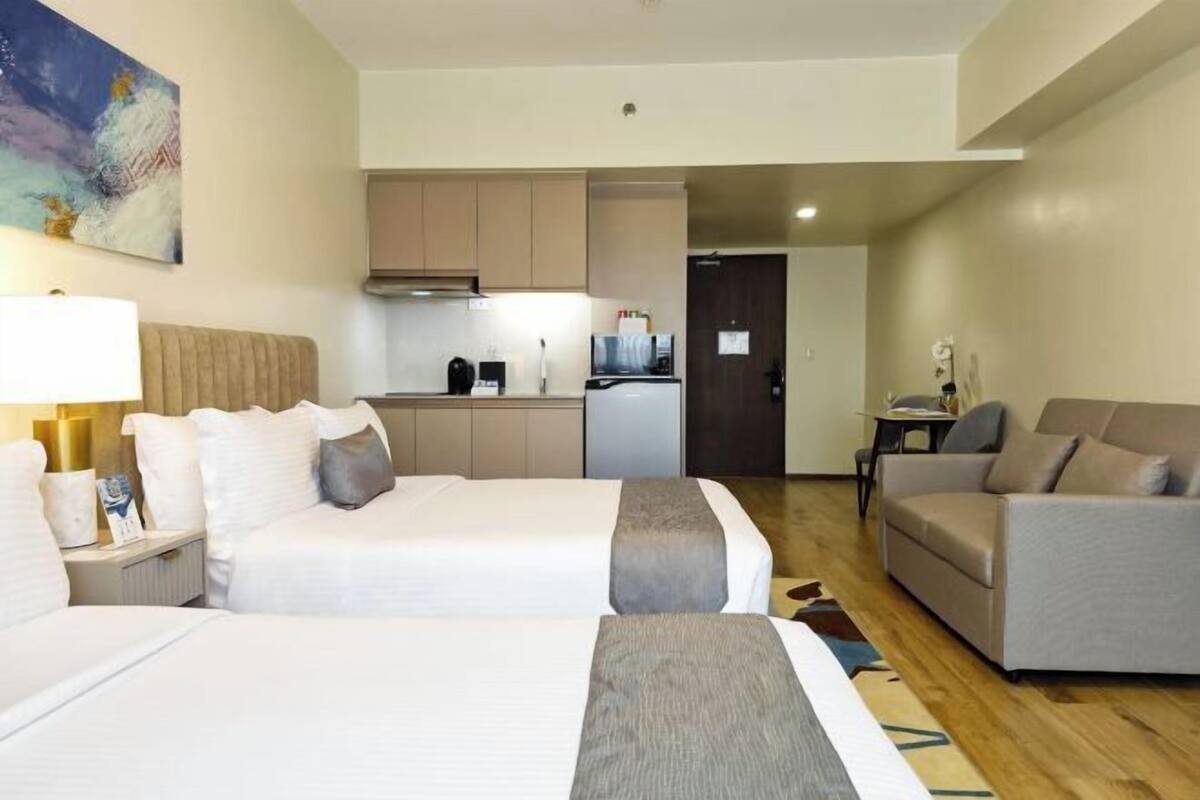 Habitación de hotel con dos camas, un sofá, una kitchenette y un cuadro en la pared.