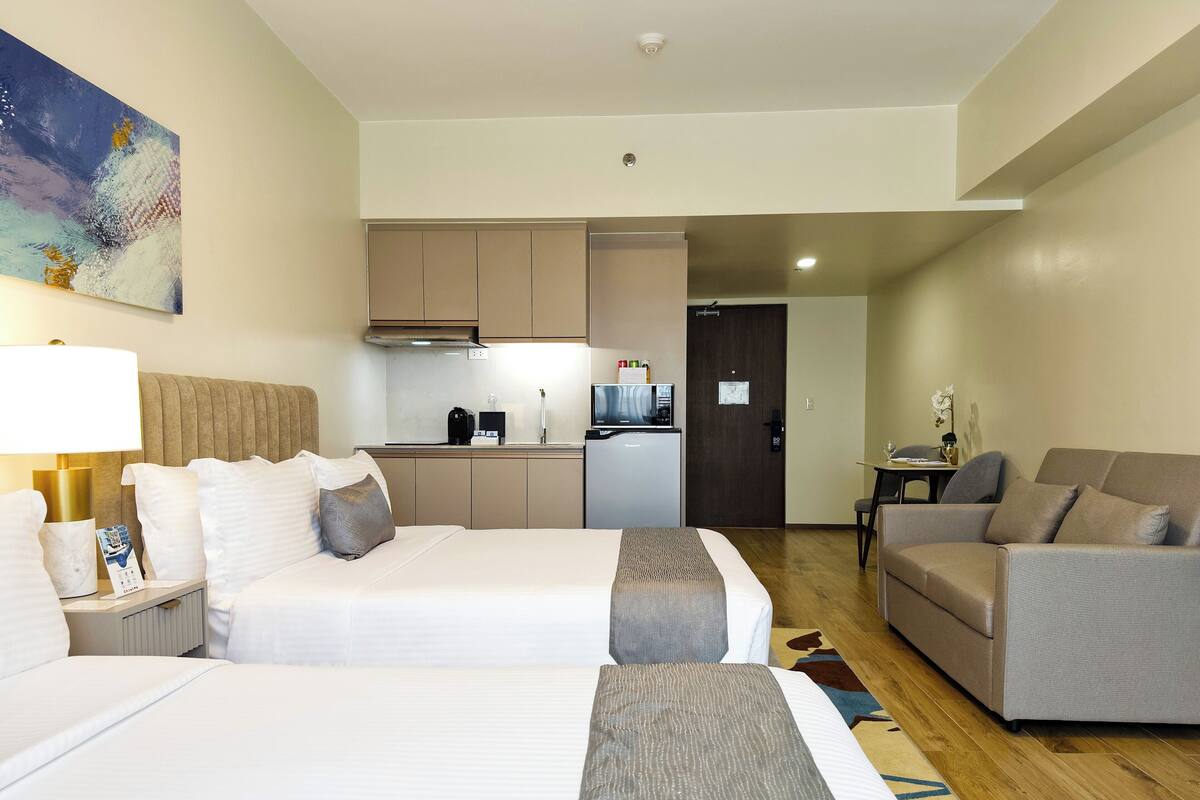 Habitación de hotel con dos camas, un sofá, una pequeña cocina y una mesa de comedor.