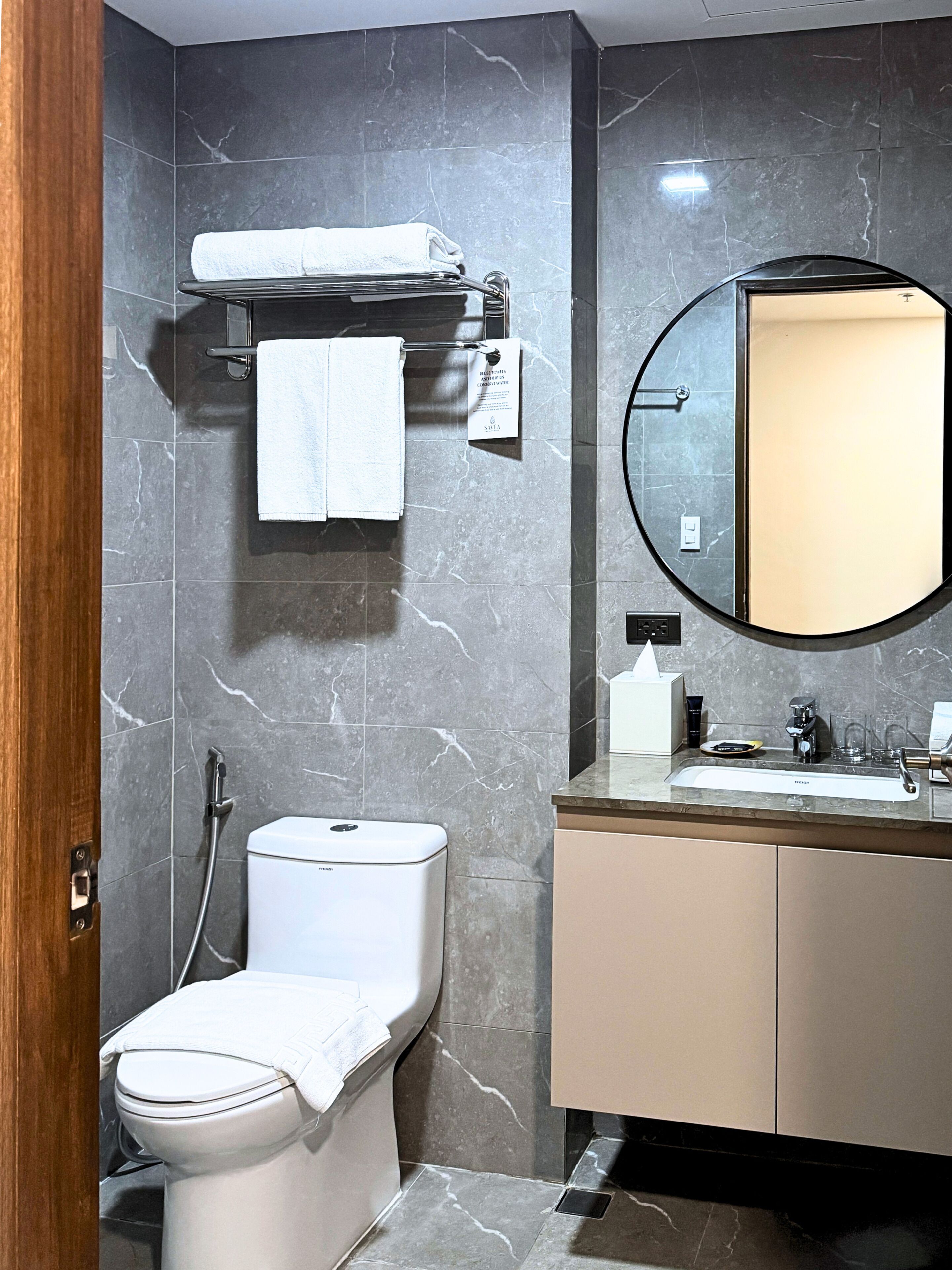Un baño moderno con inodoro, lavamanos, espejo y toallero.